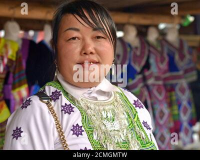 Grande femme d'affaires vietnamienne Hmong avec deux dents dorées porte une tenue traditionnelle et pose pour la caméra devant son marché de vêtements. Banque D'Images