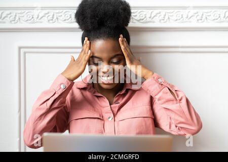 Joyeuse femme afro-américaine millénaire avec une coiffure afro porter une chemise rose regarder un film comique sur un ordinateur portable, bavarder avec des amis par appel vidéo Banque D'Images