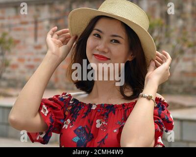 Belle jeune femme vietnamienne porte un chapeau de paille de style Amish, tient le bord du chapeau avec les deux mains, et pose pour la caméra. Banque D'Images