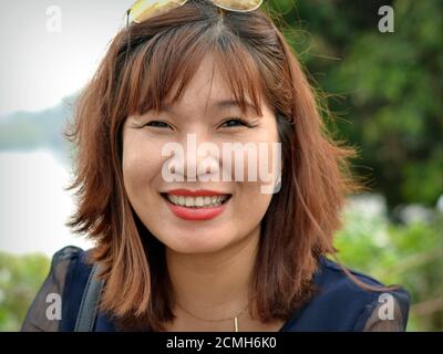 Une femme d'affaires vietnamienne réussie sourit pour l'appareil photo et montre son diamant de dent chatoyant. Banque D'Images