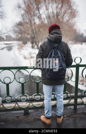 Un gars en jeans légers, bottes d'hiver marron, une veste et des casquettes rouges est muni d'un sac à dos Banque D'Images