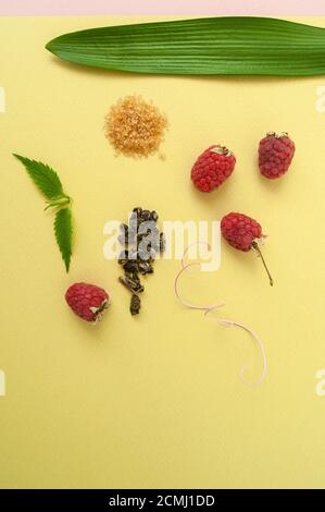 Framboises mûres, sucre, feuilles de menthe et un mélange de thé vert sur un backgrou jaune-vert pastel Banque D'Images