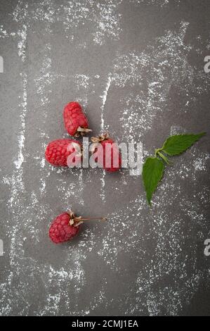 Framboises mûres et feuilles de menthe sur une table en pierre grise avec de la poudre de sucre dispersée. Banque D'Images