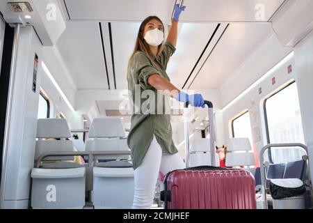 Une jeune femme portant un masque et des gants voyage avec une valise dans un train. Nouveau concept de trajet normal. Banque D'Images