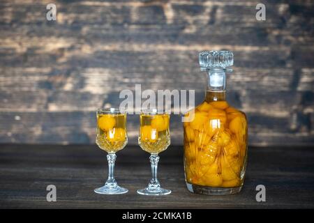 Teinture maison de prune de cerise jaune dans une bouteille de cristal et deux verres de cristal de vin sur fond de bois, Ukraine, gros plan. Baies alcoolisées Banque D'Images