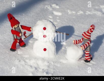 des poupées en bois en tricoté rouge roulent les boules de neige à construire un bonhomme de neige Banque D'Images