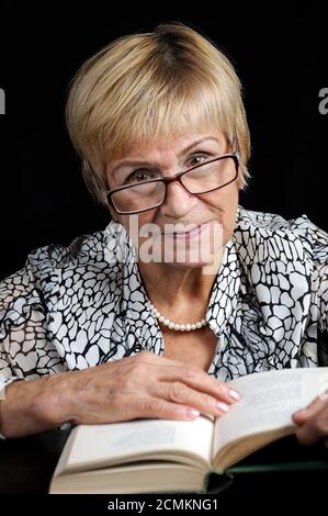 Portrait d'une femme âgée lisant un livre en lunettes sur fond noir Banque D'Images