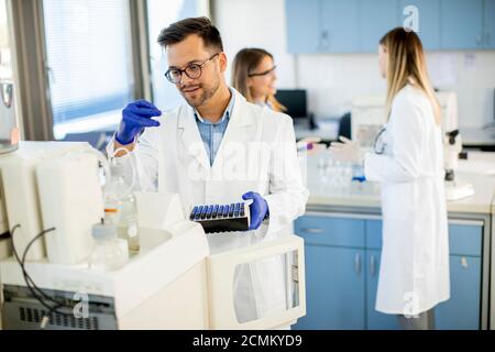 Beau chercheur en vêtements de travail de protection debout dans le laboratoire et analyse d'échantillons liquides Banque D'Images