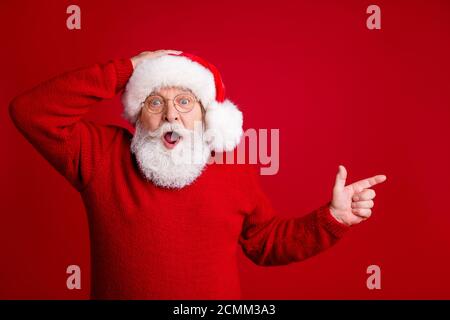 Photo d'un vieil homme aux cheveux gris émerveillés au père noël chapeau point index copyspace impressionné jolly holly x-mas ads pull promo wear isolé Banque D'Images