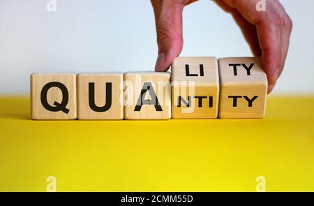 Qualité sur quantité. La main fait tourner les cubes et change le mot « quantité » en « qualité ». Belle table jaune, fond blanc, espace de copie. Activité c Banque D'Images