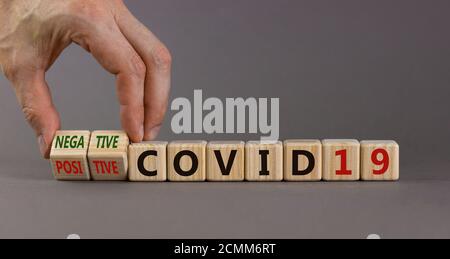 Résultat d'un test Corona. La main masculine fait tourner un cube et change l'expression 'positive COVID19' en 'négative COVID19'. Magnifique fond gris. M Banque D'Images