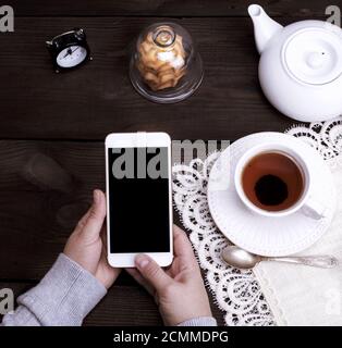 Deux mains tenant un smartphone blanc avec un écran noir vide Banque D'Images