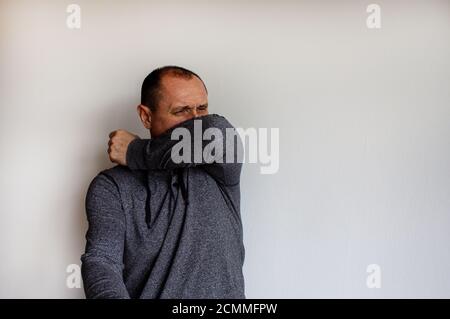 Gros plan portrait tête pétrifié jeune homme beau éternuant sur le coude, arrière-plan blanc isolé. Banque D'Images