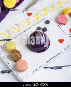 Gâteau rond lilas avec des macarons sur une planche de bois blanc Banque D'Images