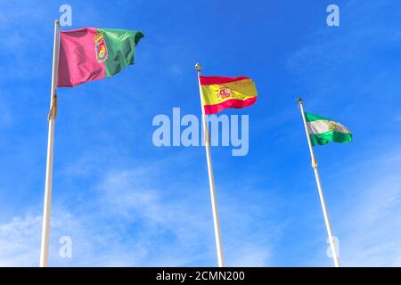 Drapeaux de l'Andalousie, de Grenade et de l'Espagne, agitant dans un ciel nuageux. Fond ciel libre pour un espace de copie et un soleil éclatant. Banque D'Images