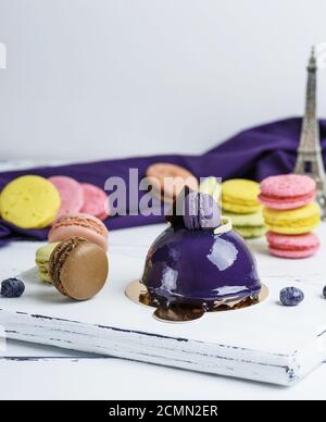 Gâteau rond lilas avec des macarons sur une planche de bois blanc Banque D'Images