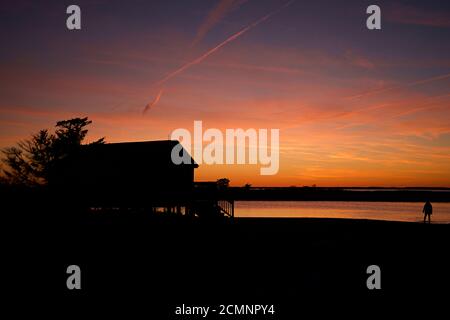 Coucher de soleil sur l'île d'Assateague au-dessus des marais, baie d'eau salée avec silhouette de bâtiment et arbres près du bord de l'eau. Banque D'Images