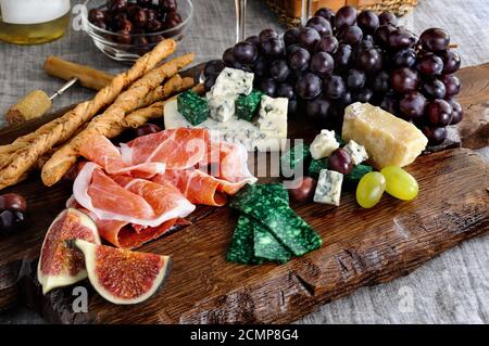 Plats pour une collation Antipasto sur une planche de bois avec prosciutto, différentes sortes de fromages, raisins et Banque D'Images