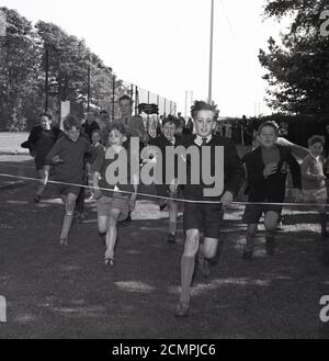 Années 1960, histoire, temps d'été et à l'extérieur sur une zone d'herbe, des garçons de différents âges, certains dans leur uniforme scolaire, avec des cravates et des vestes, en compétition dans une course à pied à une tête d'école, avec le garçon gagnant sur le point de frapper la bande d'arrivée, Bowhill, Écosse. Banque D'Images