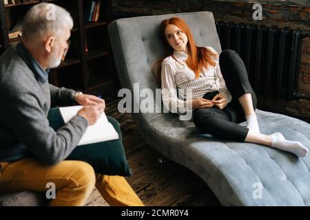 Professionnel homme senior psychologue écoutant le patient et prenant des notes sur le presse-papiers. Banque D'Images