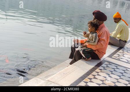 Amritsar, Inde - 21 novembre 2011 : une famille de pèlerins sikhs, père et fils, sont assis près d'un lac dans le complexe du Temple d'Or. Amritsar, Punjab Banque D'Images
