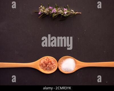 Cuillères en bois avec du sel marin et rose de l'himalaya sels et d'une brindille de romarin sur une plaque en ardoise Banque D'Images