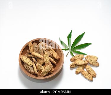 Biscuits sablés croustillants aux graines de cannabis dans une assiette en bois sur fond blanc Banque D'Images