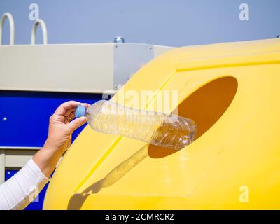 A mature woman pulling une bouteille en plastique dans un bac en plastique jaune pour recyclage Banque D'Images