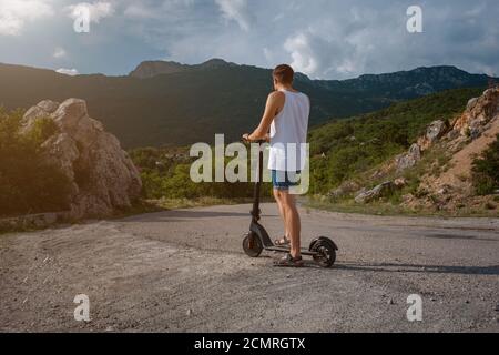 Jeune homme à bord d'un scooter électrique sur la chaîne de montagnes. Concept de transport écologique Banque D'Images