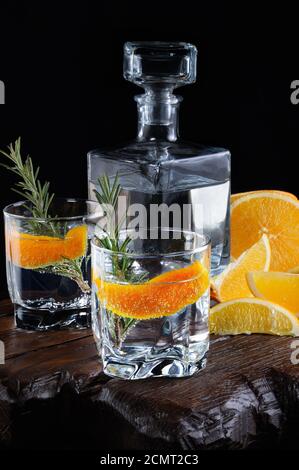 Cocktail classique de gin sec avec tonique et zeste d'orange avec une branche de romarin sur une planche de bois avec Banque D'Images