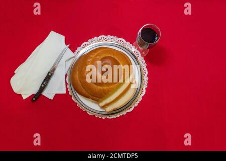 Pain à la challah rond avec verre de vin, serviette et couteau sur nappe rouge. Nourriture juive traditionnelle pour le Sabbat et les vacances. Copier l'espace. Banque D'Images