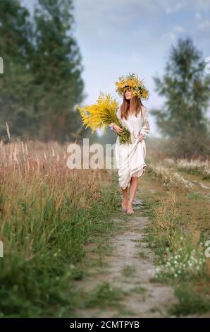 Belle fille dans une couronne de fleurs sauvages et un ancien vêtements brodés avec un grand bouquet marchant pieds nus sur le chemin. Vacances à Ivana Kupala Banque D'Images