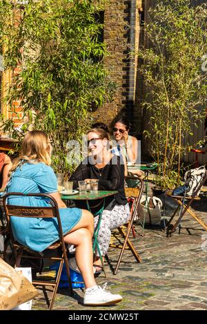 Londres, Royaume-Uni - 13 septembre 2020 : marché du dimanche des fleurs de Columbia Road. Les jeunes femmes discutent à la table de café extérieure Banque D'Images