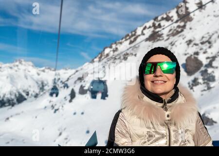 Jeune adulte beau heureux attrayant caucasien souriant femme aiment l'ascension assis à l'intérieur du télécabine contre la station de ski panorama Banque D'Images