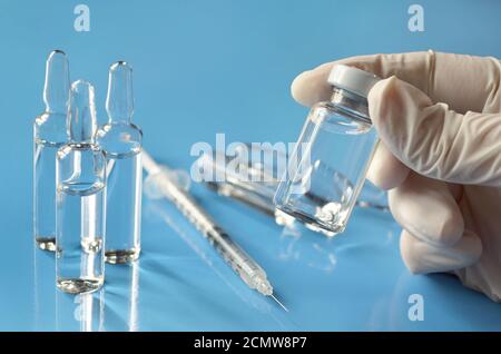 Flacon médical de médicament dans les mains d'un professionnel de la santé sur fond bleu clair avec des ampoules en verre et une seringue jetable. Banque D'Images