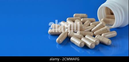 Heap Pills-capsules avec un contenant médical blanc sur fond bleu avec espace de copie, foyer sélectif. Concept de soins de santé. Banque D'Images