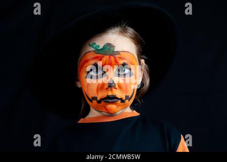 Triste fille avec maquillage de citrouille sur son visage pour Halloween, dans un chapeau noir, solitude et tristesse en vacances Banque D'Images