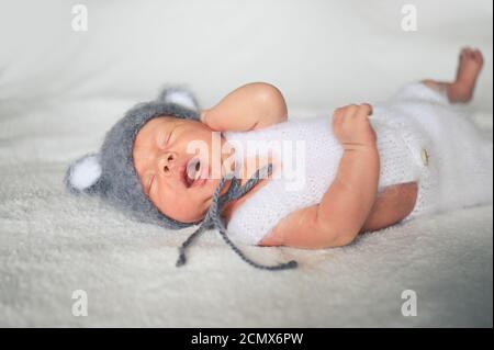 Mignon nouveau-né pleurs petit garçon dormant dans un lit de bébé dans un costume tricoté avec des oreilles. Modèle d'emballage pour bébés. Enfant en bonne santé, concept d'hôpital Banque D'Images