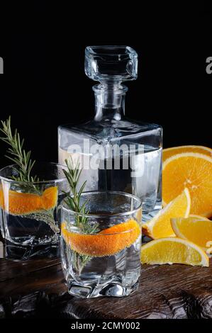 Cocktail classique de gin sec avec tonique et zeste d'orange avec une branche de romarin sur une planche de bois avec Banque D'Images