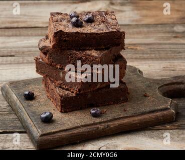 pile de tranches carrées de gâteau au chocolat au brownie avec noix sur une surface en bois. Cuit à la maison Banque D'Images