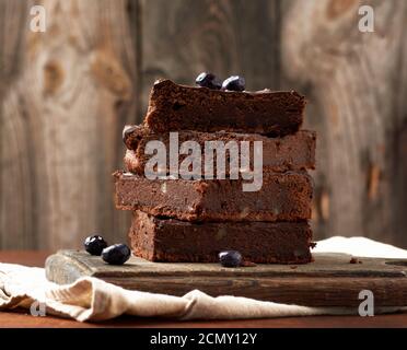 pile de tranches carrées de gâteau au chocolat au brownie avec noix sur une surface en bois. Cuit à la maison Banque D'Images