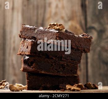 pile de tranches carrées de gâteau au chocolat au brownie avec noix sur une surface en bois. Cuit à la maison Banque D'Images