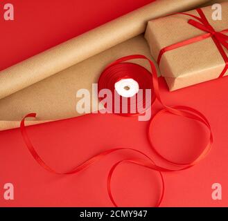 papier d'emballage, un rouleau de ruban rouge et un cadeau emballé dans du papier kraft brun Banque D'Images