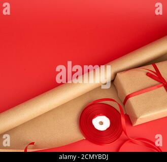papier brun pour l'emballage, un rouleau de ruban rouge et un cadeau emballé dans du papier kraft brun Banque D'Images