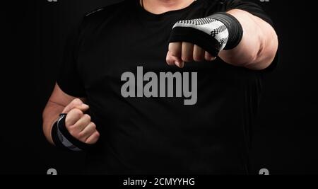 homme adulte en uniforme noir et bras musclés debout dans une position sportive, tient une interdiction élastique sportive Banque D'Images