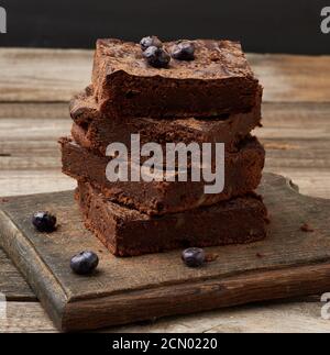 pile de tranches carrées de gâteau au chocolat au brownie avec noix sur une surface en bois. Cuit à la maison Banque D'Images