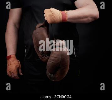athlète musclé en uniforme noir tient très vieux brun gants de boxe dans la main Banque D'Images