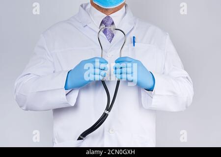 le médecin en manteau blanc et cravate tient dans sa main un phonendoscope noir, portant des gants stériles bleus Banque D'Images