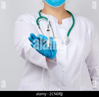 femme medic en manteau blanc et gants en latex bleu tenant une seringue, fond blanc studio Banque D'Images