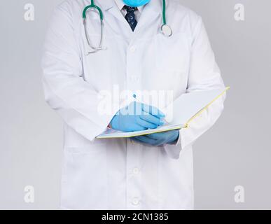 docteur en robe blanche, gants stériles en latex bleu tient un carnet jaune ouvert dans sa main sur un coup Banque D'Images